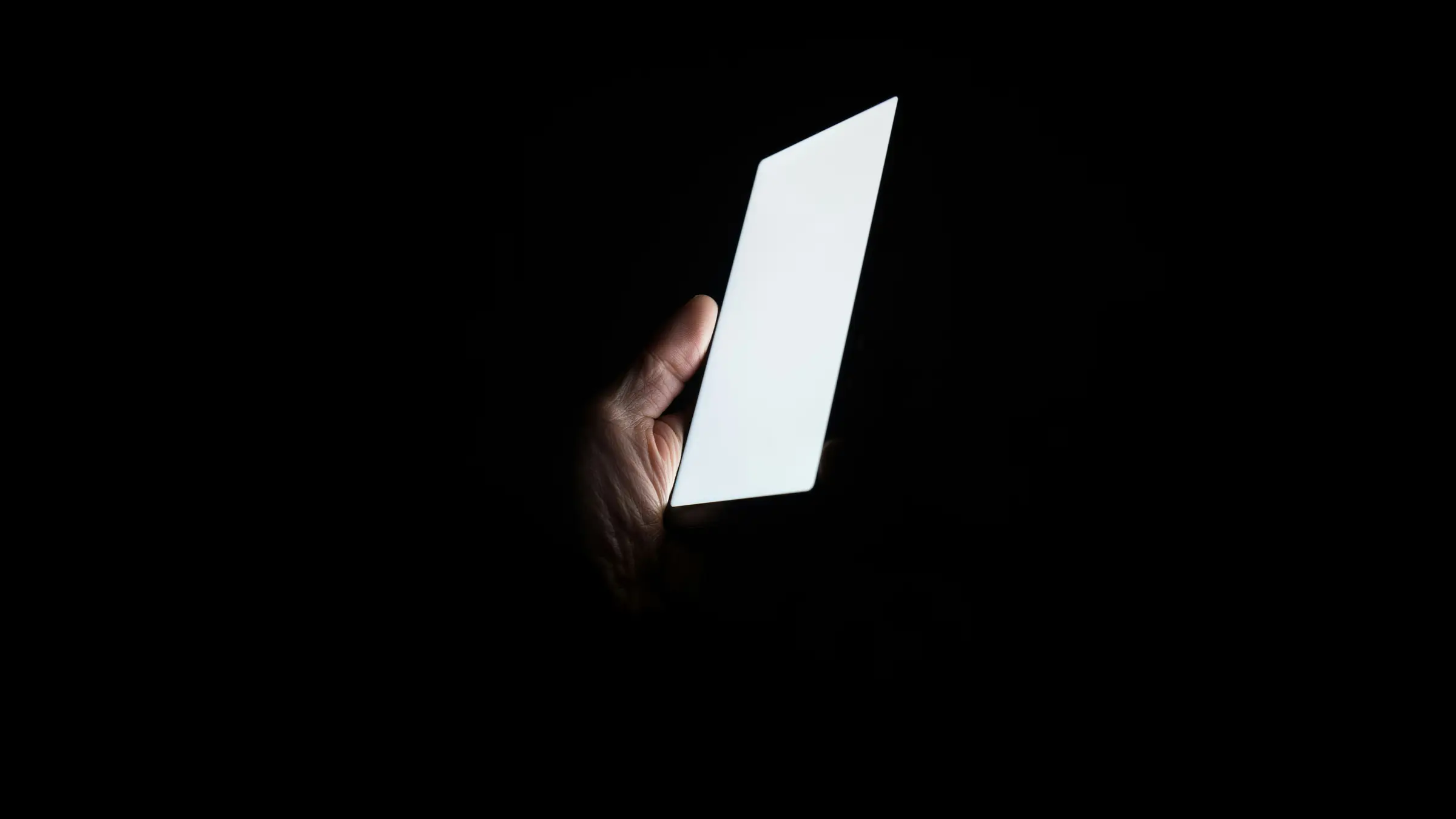 Mano con un celular encendido en la oscuridad